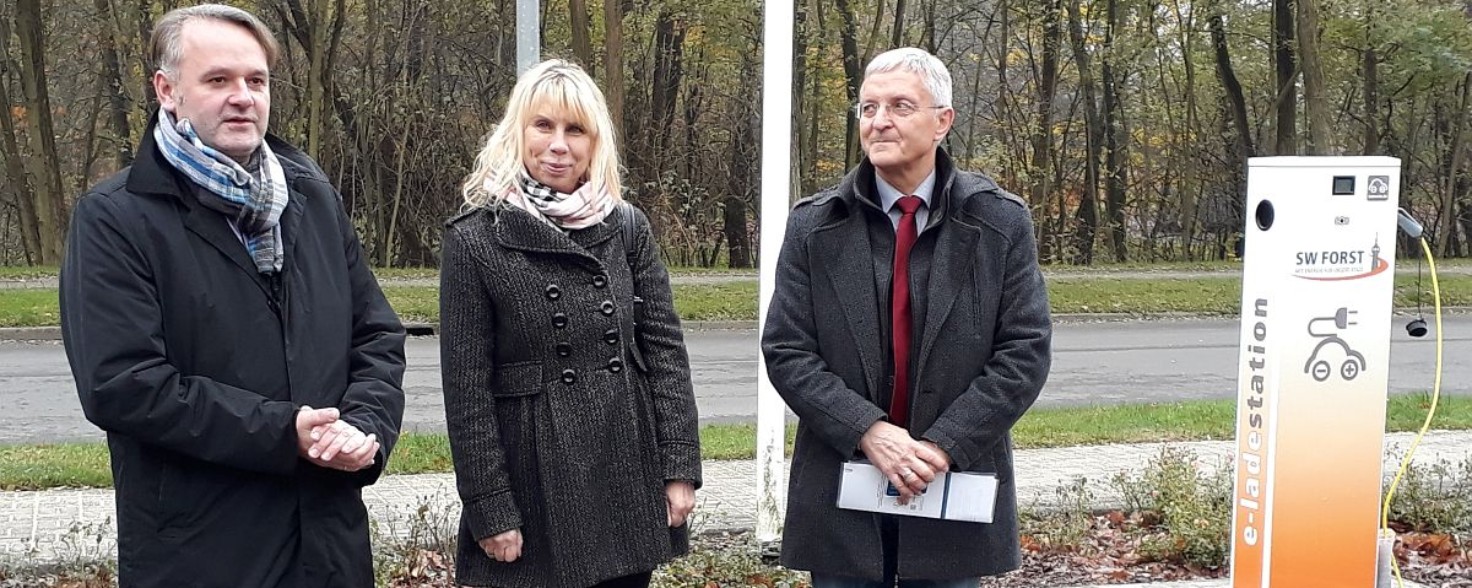 Zwei Männer und eine Frau stehen neben einer Elektroauto-Ladestation