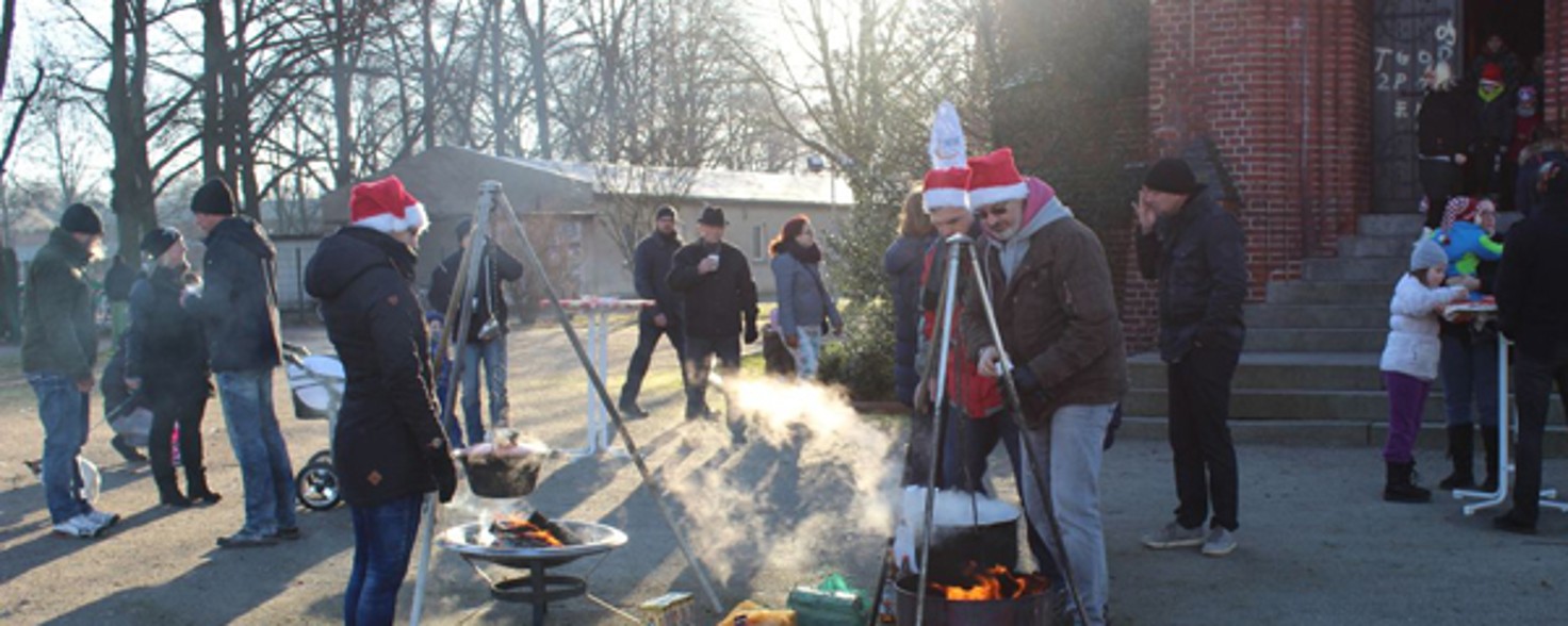 Eine Gruppe Menschen steht um zwei Grills herum. Dabei tragen sie Weihnachtsmützen.