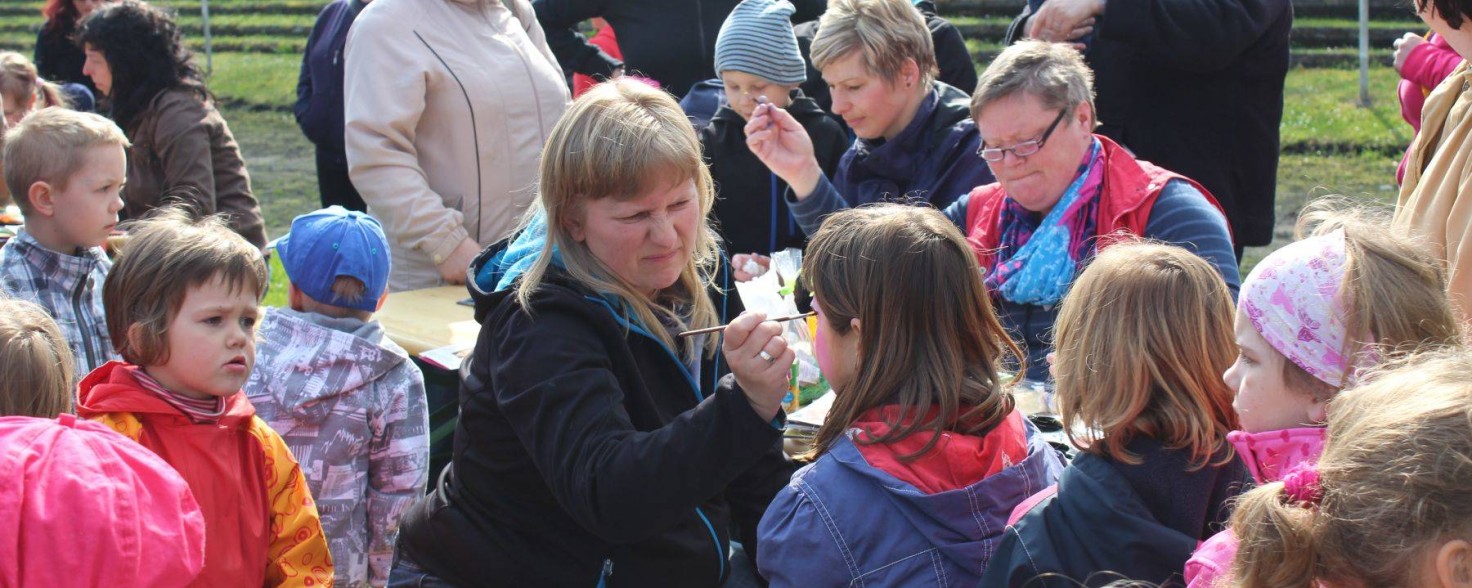 Mehrere Frauen und Kinder sitzen auf Bänken, während eine Frau ein Mädchen schminkt