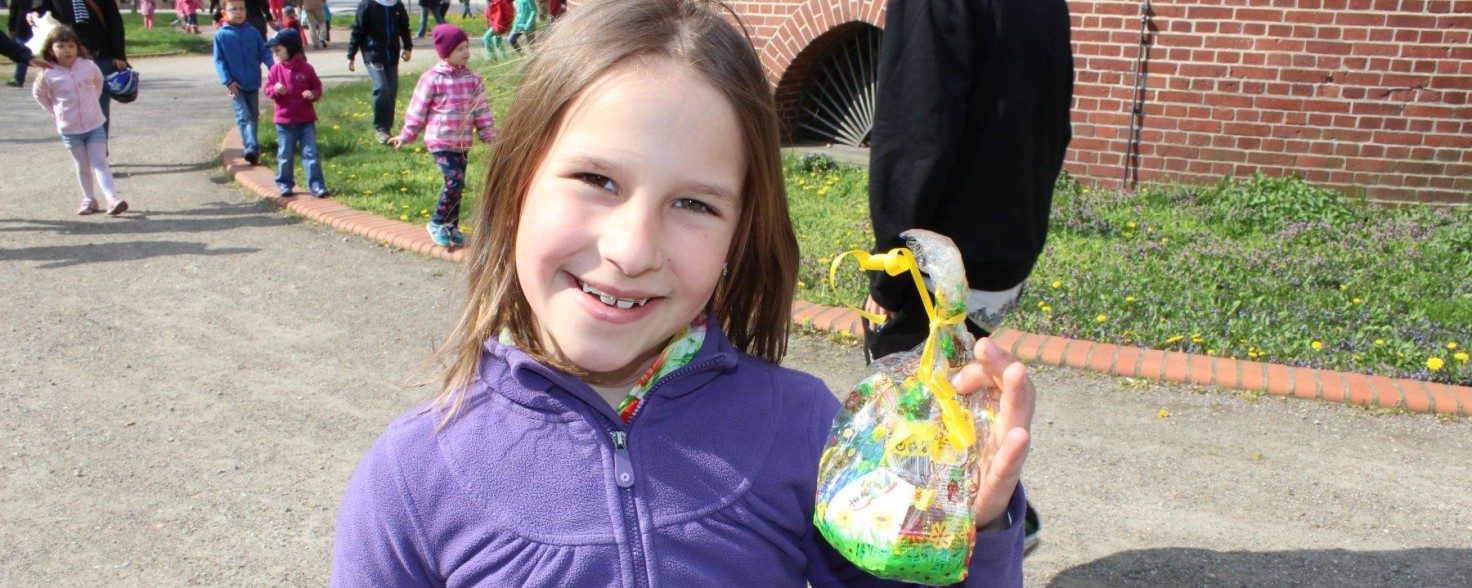 Ein Mädchen in violetter Jacke hält ein Päkchen mit Ostereiern in die Kamera und lächelt