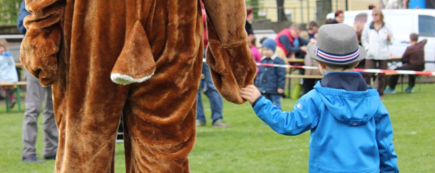 Ein Mensch im Hasenkostüm läuft Hand in Hand mit einem kleinen Jungen in blauer Jacke