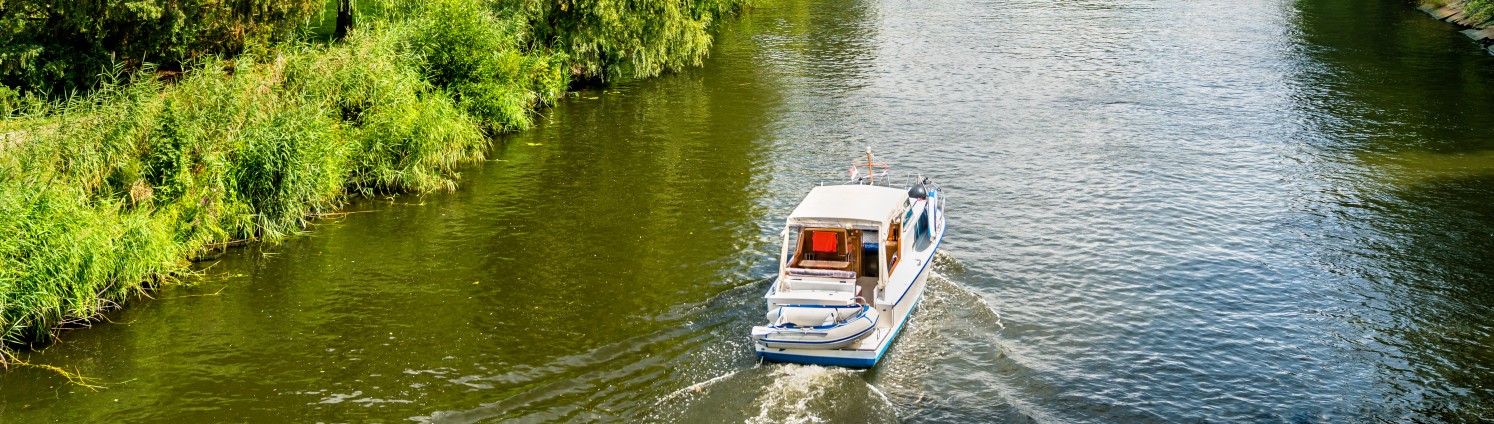 Ein Boot fließt auf einem Fluss entlang, in der Ferne steht ein Turm