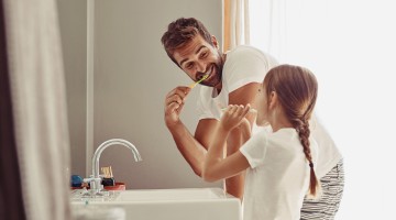 Ein Mann putzt mit seiner Tochter die Zähne im Bad