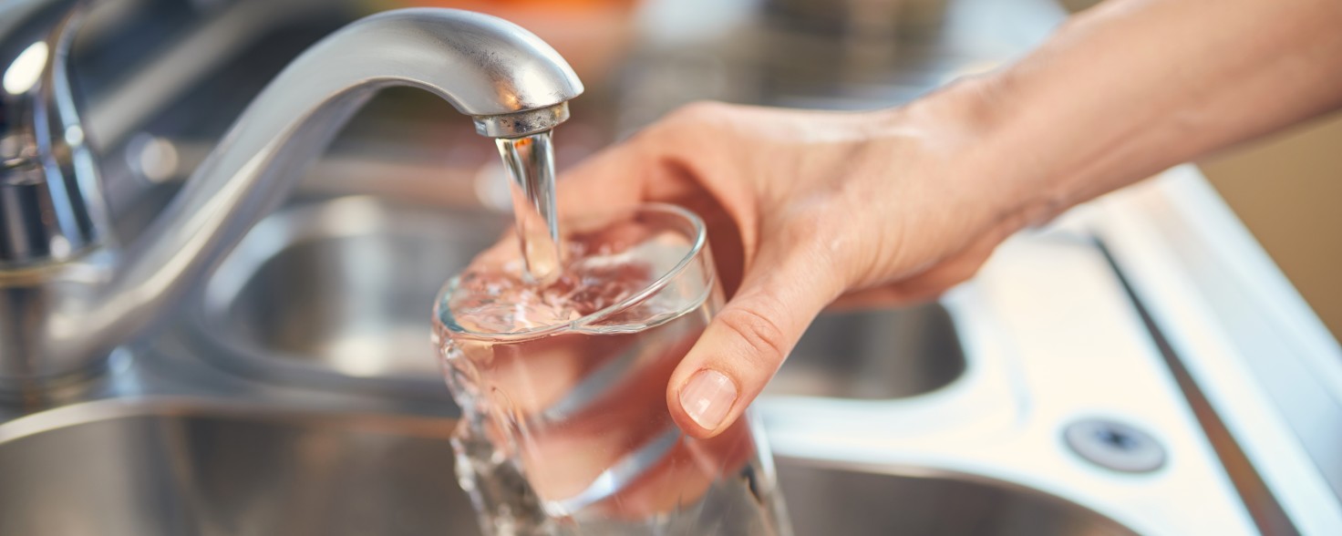 Ein Glas wird unter einen Wasserhan gehalten